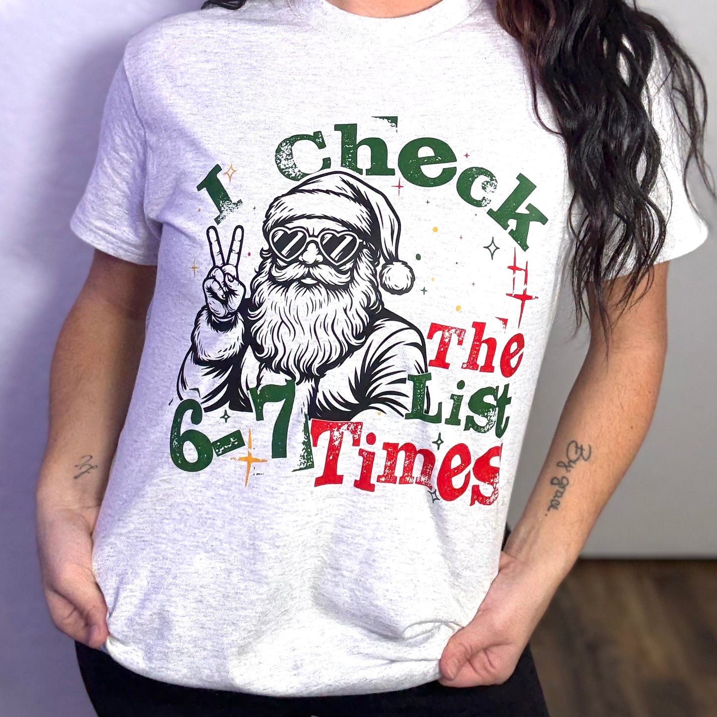 Person wearing a white t-shirt with a graphic of Santa Claus and text 'I Check The List 6-7 Times'.