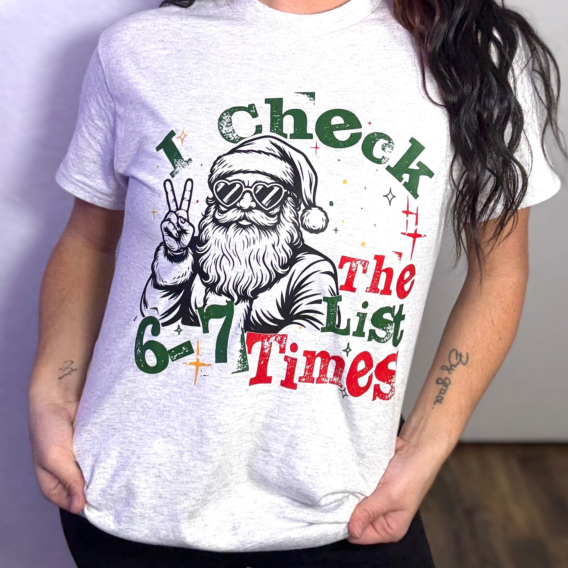 Person wearing a white t-shirt with a graphic of Santa Claus and text 'I Check The List 6-7 Times'.